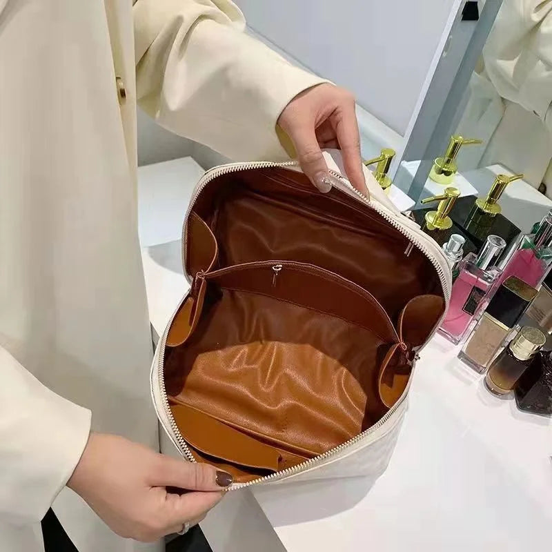 White toiletry bag for women, Fancy material and look, Metal zipper, Top view, Inside pockets, Women's' hand holding it open, Opened toiletry bag to show the lined inside, Bag sitting on table in bedroom in front of mirror, Lifestyle image