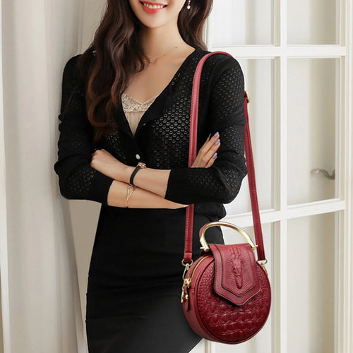 Fancy looking woman arms crossed smiling, using shoulder strap for a red leather crossbody bag, in front of white door with glass